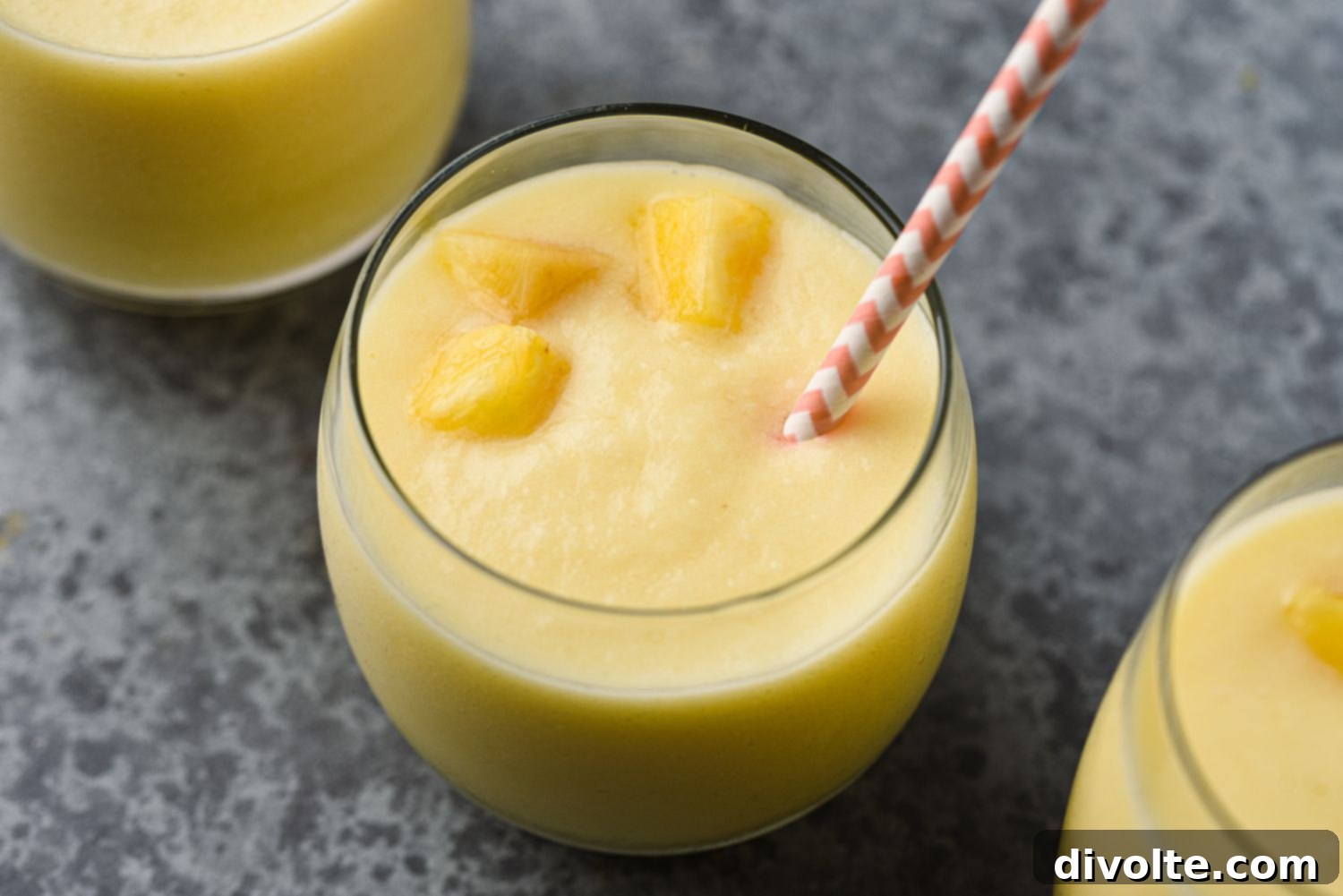 pineapple-coconut-smoothie-recipe - a glass of creamy pineapple coconut smoothie garnished with a small slice of pineapple and a straw