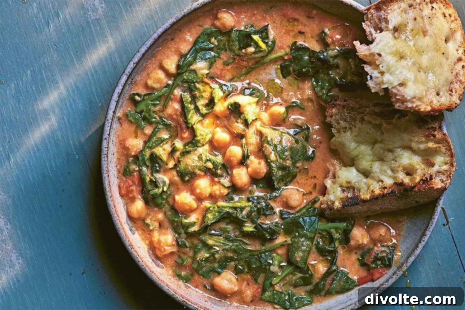 chickpea-spinach-stew-recipe - A comforting bowl of vibrant chickpea spinach stew with crusty bread on the side.