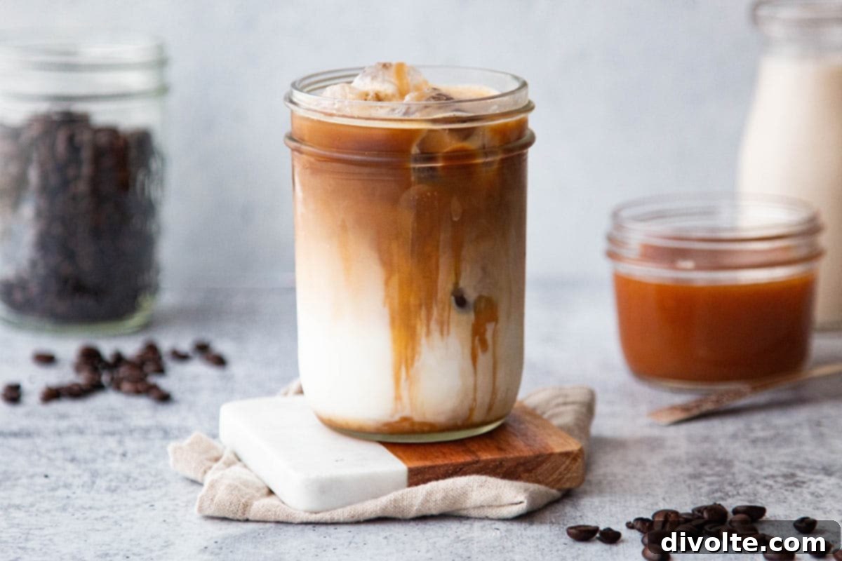 Easy Homemade Iced Caramel Macchiato 2 A tall glass of homemade iced caramel macchiato featuring distinct layers of cold milk, dark espresso, and a golden caramel drizzle, garnished with a coffee bean, set against a bright, inviting background.
